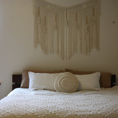 The Family Bedroom - the cozy nook,king bed dressed in textured cream bedding, plush pillows, and a round woven accent pillow, with a large cream macrame wall hanging displayed above on a beige wall.